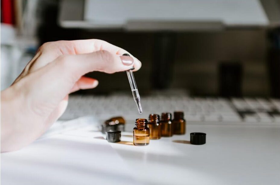 About Hand using a glass dropper to apply natural body oil into amber glass bottles, representing New Roots Grooming Co. body oil collection